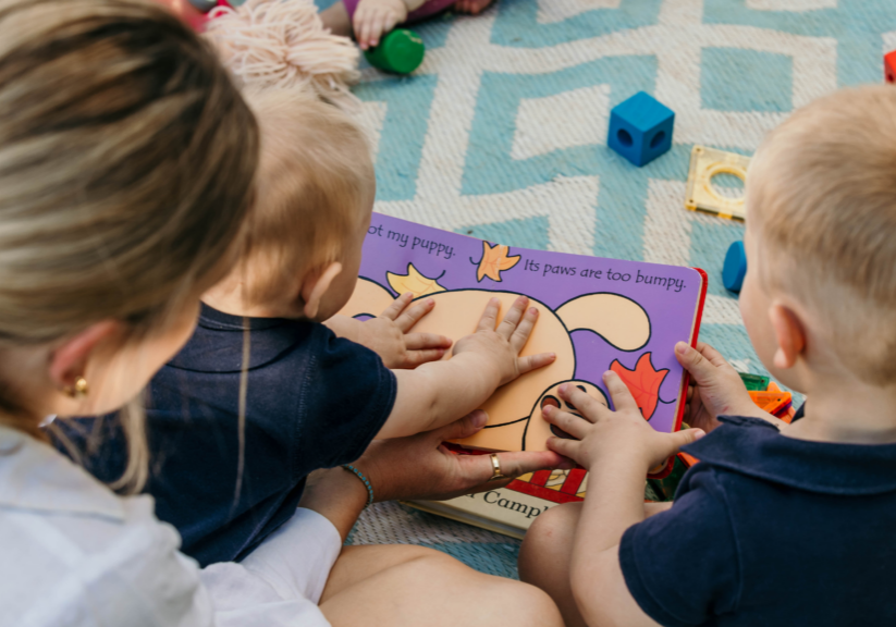 Parent reading a storybook with a young child while looking at colourful picture book illustrations together. Show more lines