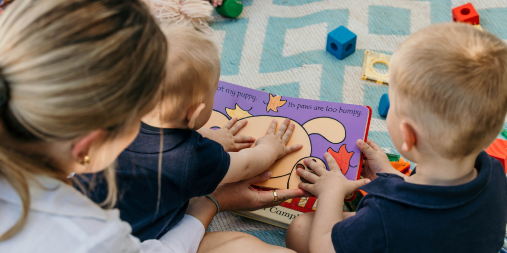 Parent reading a storybook with a young child while looking at colourful picture book illustrations together. Show more lines